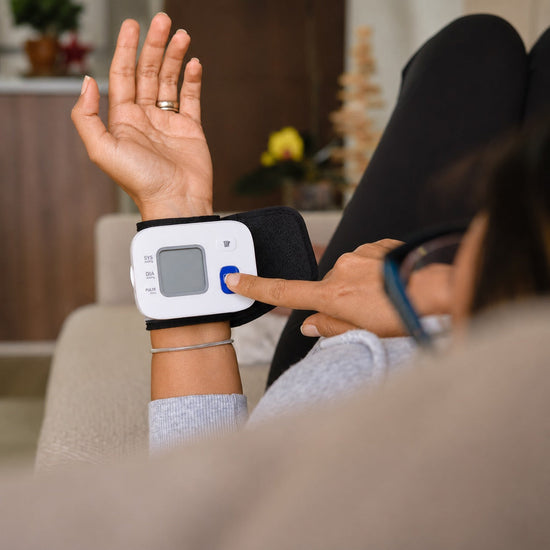 Woman pressing button on digital wrist blood pressure monitor at home